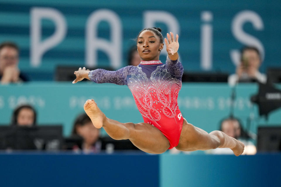 Simone Biles performs a lunge during a gymnastics competition in Paris. She is wearing a shiny athletic outfit