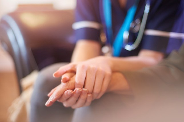 A nurse comforts a patient in the hospital, holding their hand